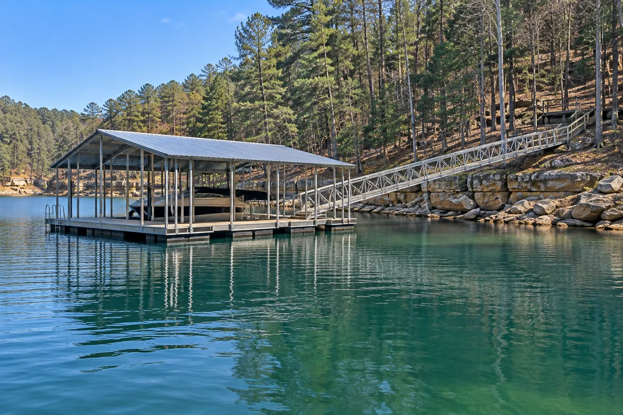 A new floating boathouse with open sides and a metal roof, joined to a wooded shore by a long walkway